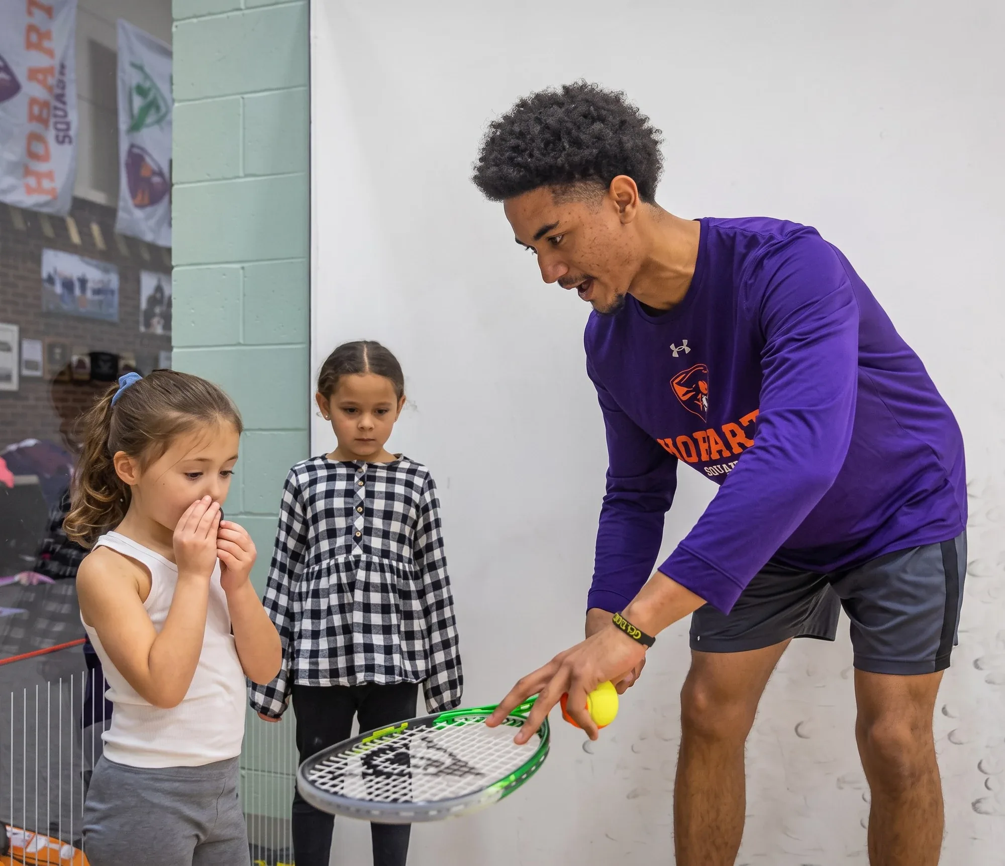 Coach Raji Davenport teaching a group of young children on a squash court